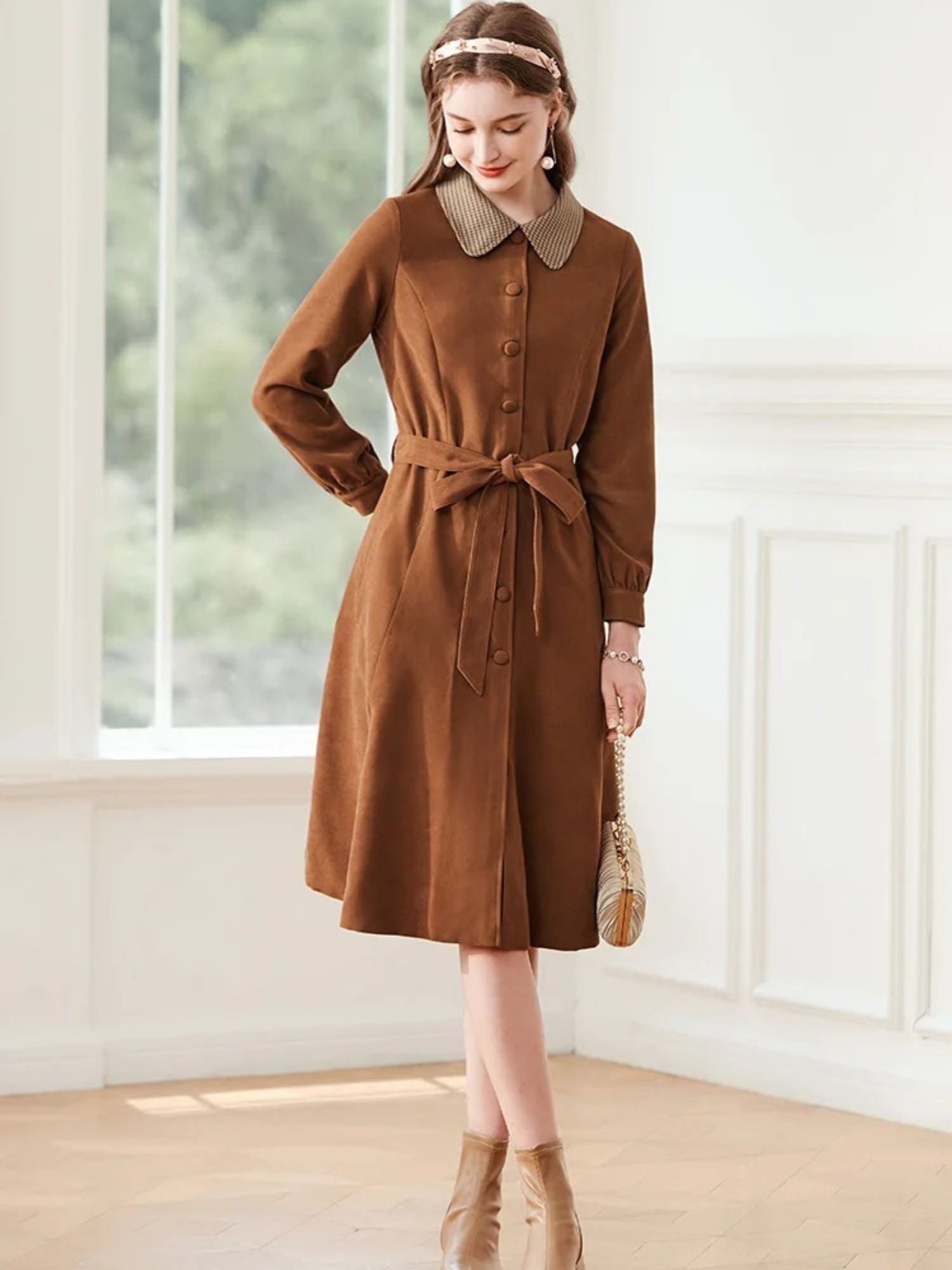 A woman wearing a brown A-line dress with a turn-down collar, long sleeves, front button closure, and tie waist.