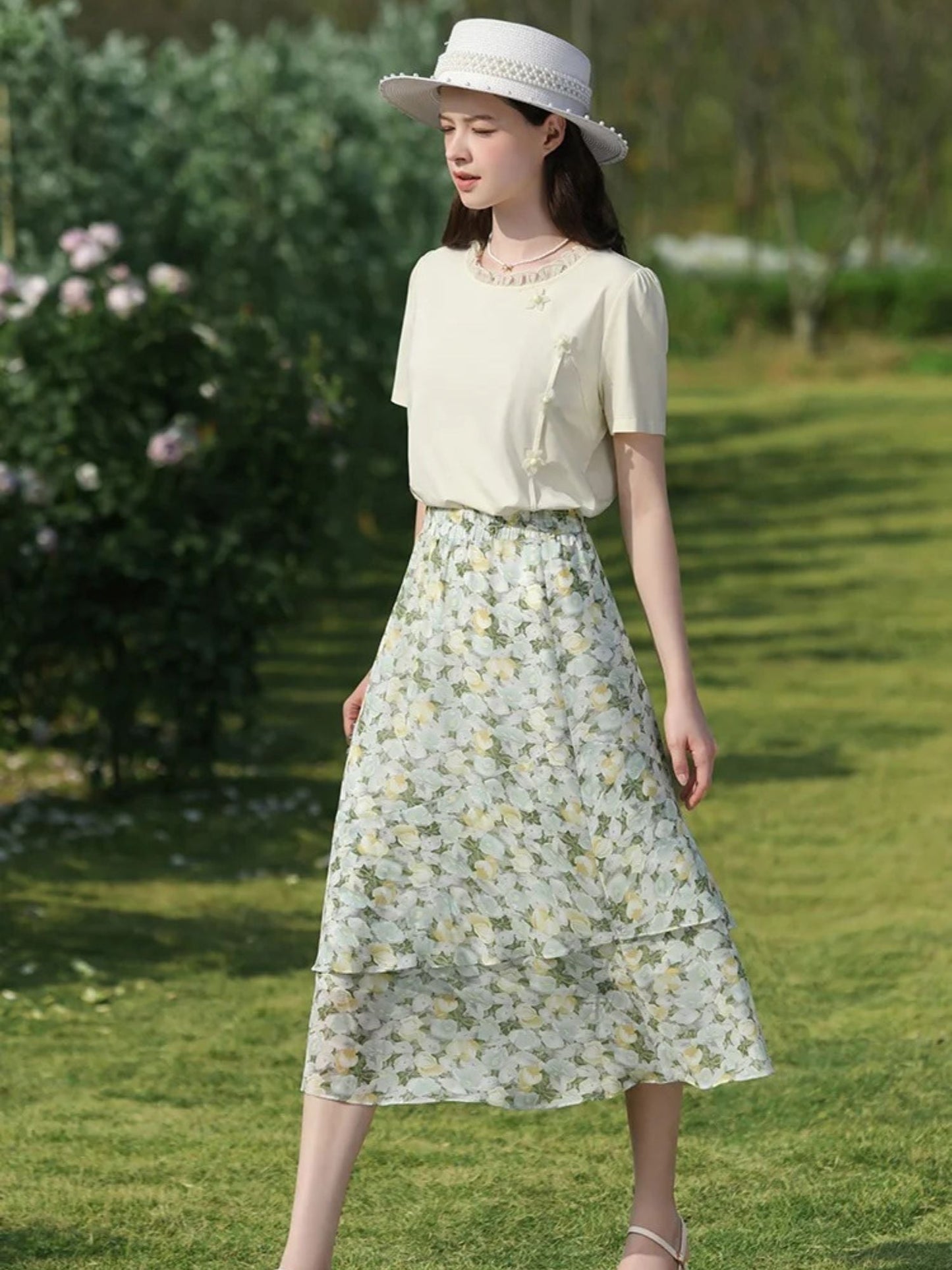 A woman wearing a floral chiffon midi skirt with a high elastic waistband, paired with a plain top, standing in a garden.