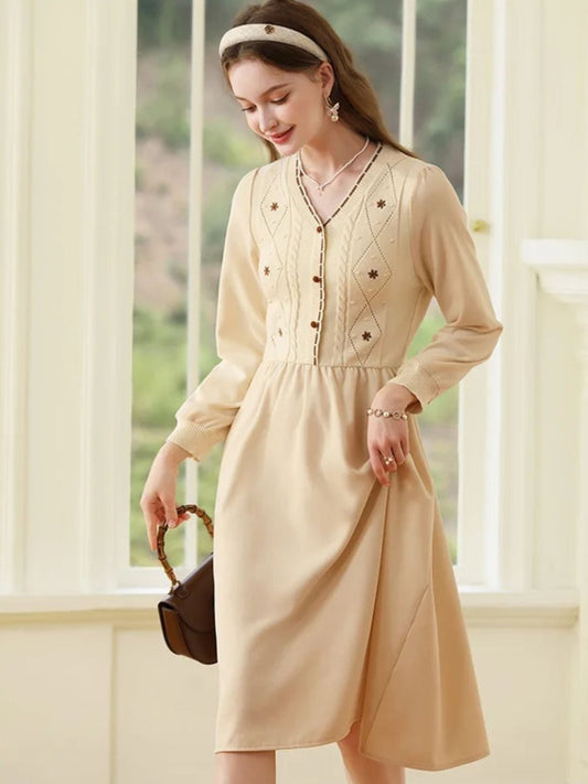 A beige A-line midi dress with long sleeves, V-neckline, and front button closure featuring embroidery on the bodice.