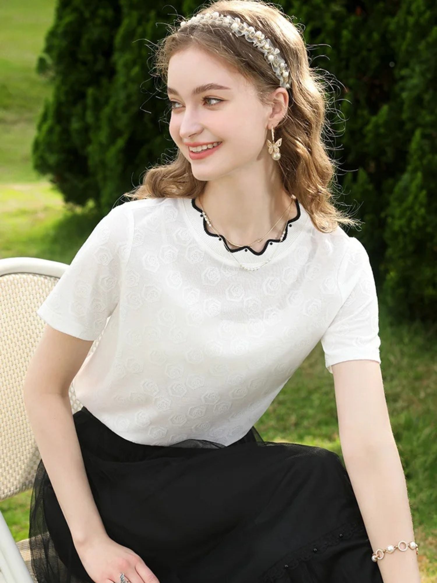 A woman wearing a white short-sleeved blouse with embroidered lace and a crew neckline, paired with a black skirt.