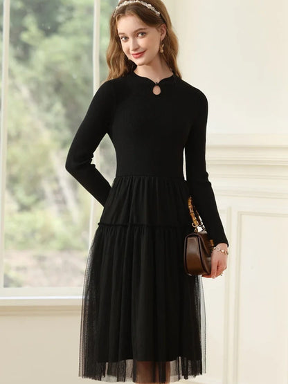 A woman wearing a long-sleeved, knee-length black dress with a tiered tulle skirt and a round neckline with a keyhole detail.