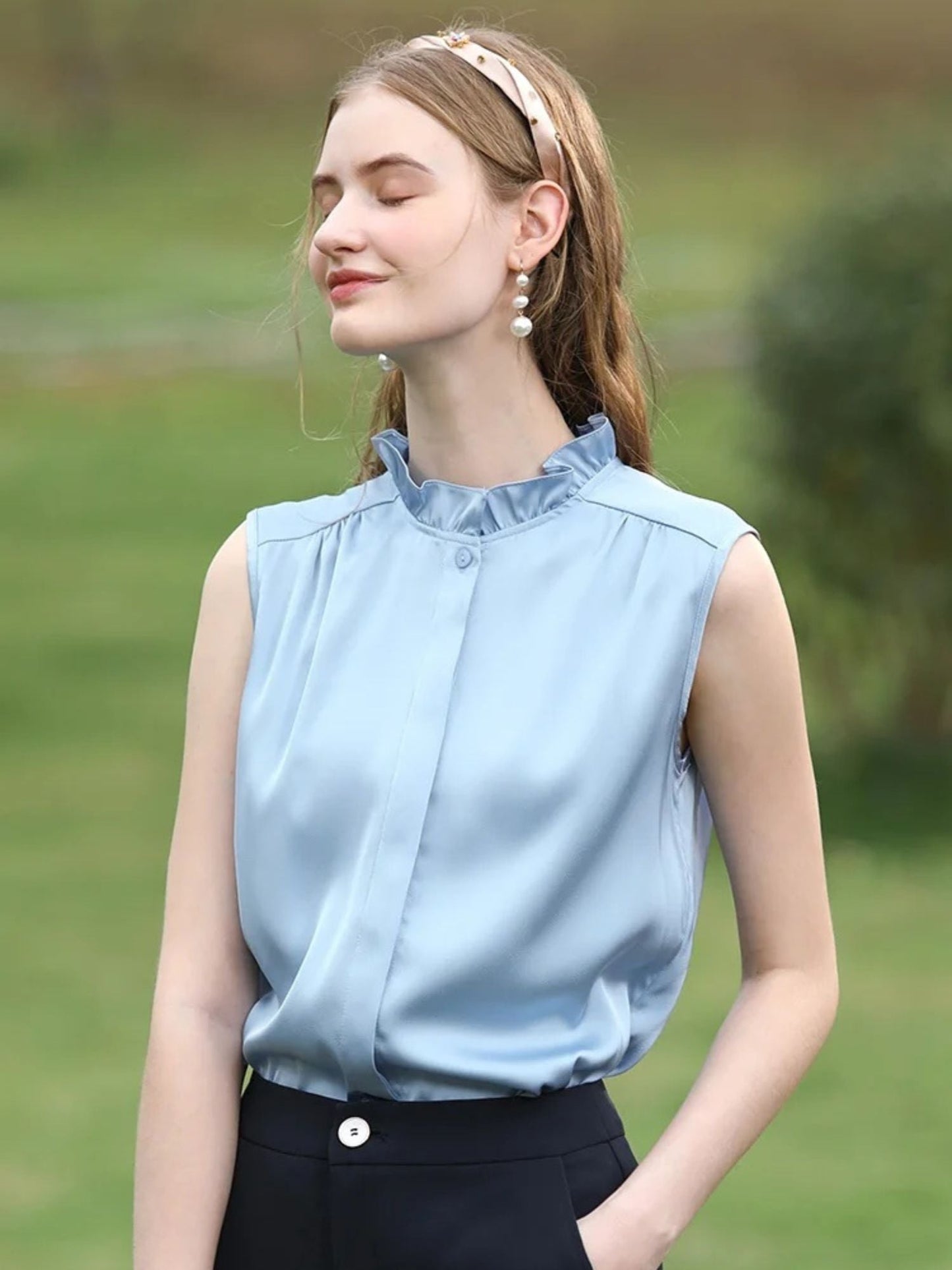 A woman wearing a sleeveless blouse with a ruffled collar design.
