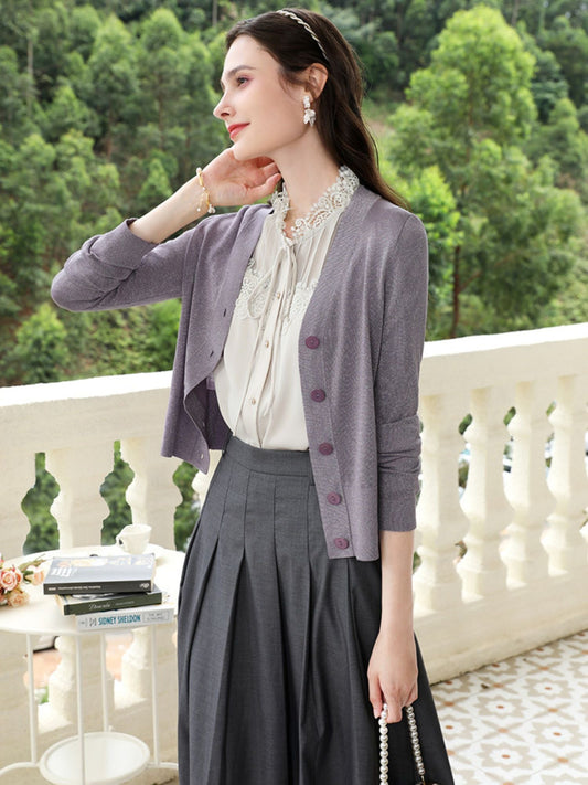 A woman wearing a French-inspired lightweight knit cardigan in purple, with a V-neckline and single-breasted button front. She is also wearing a white shirt and gray skirt.