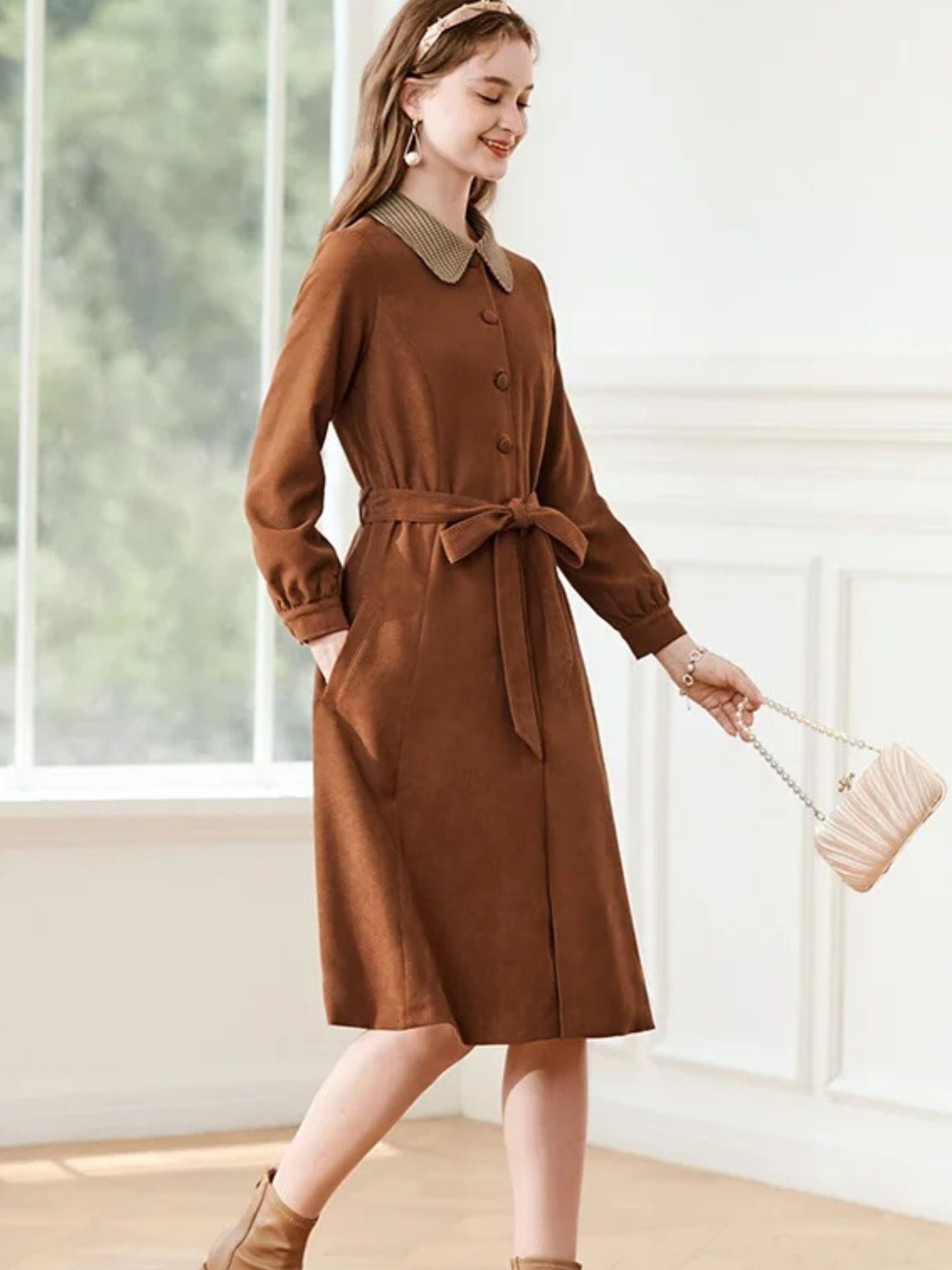 A woman wearing a brown A-line dress with a turn-down collar, long sleeves, front button closure, and tie waist.