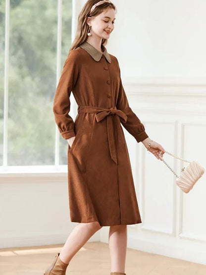A woman wearing a brown A-line dress with a turn-down collar, long sleeves, front button closure, and tie waist.