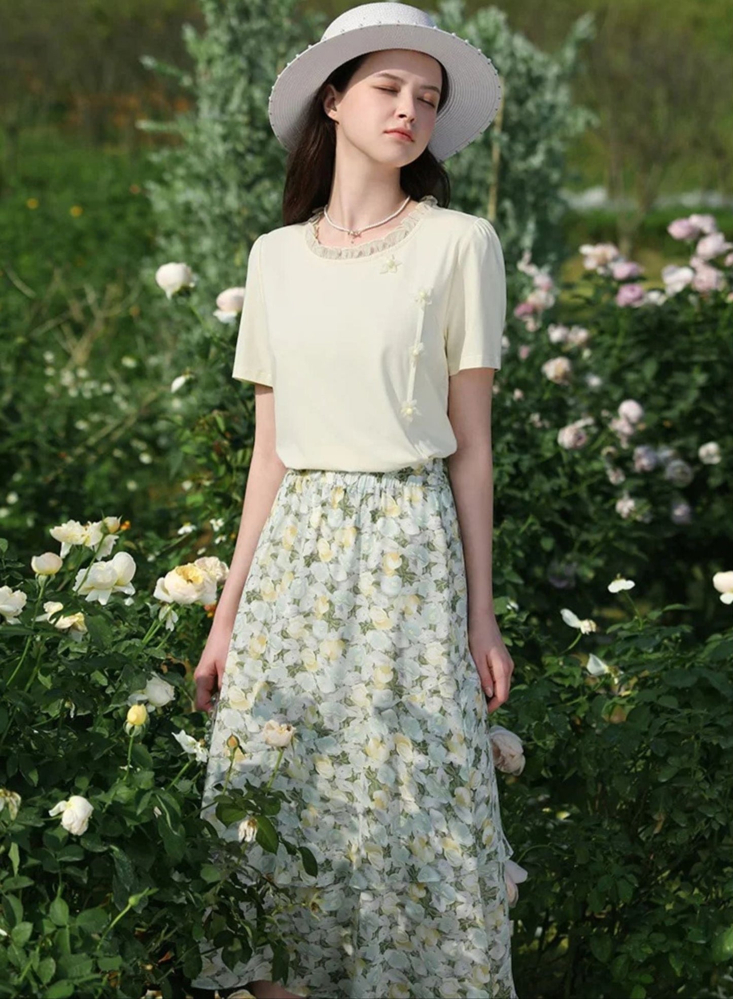 A woman wearing a floral chiffon midi skirt with a high elastic waistband, paired with a plain top, standing in a garden.