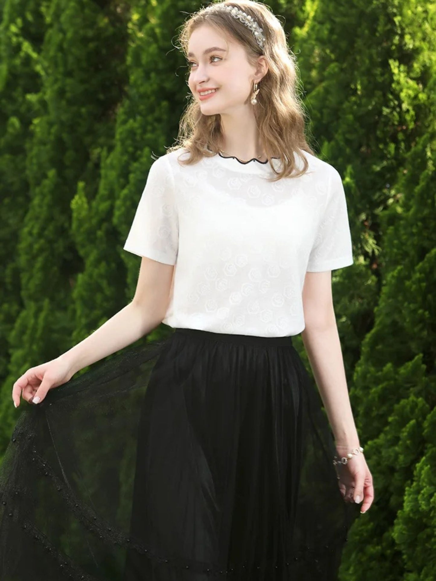 A woman wearing a white short-sleeved blouse with embroidered lace and a crew neckline, paired with a black skirt.