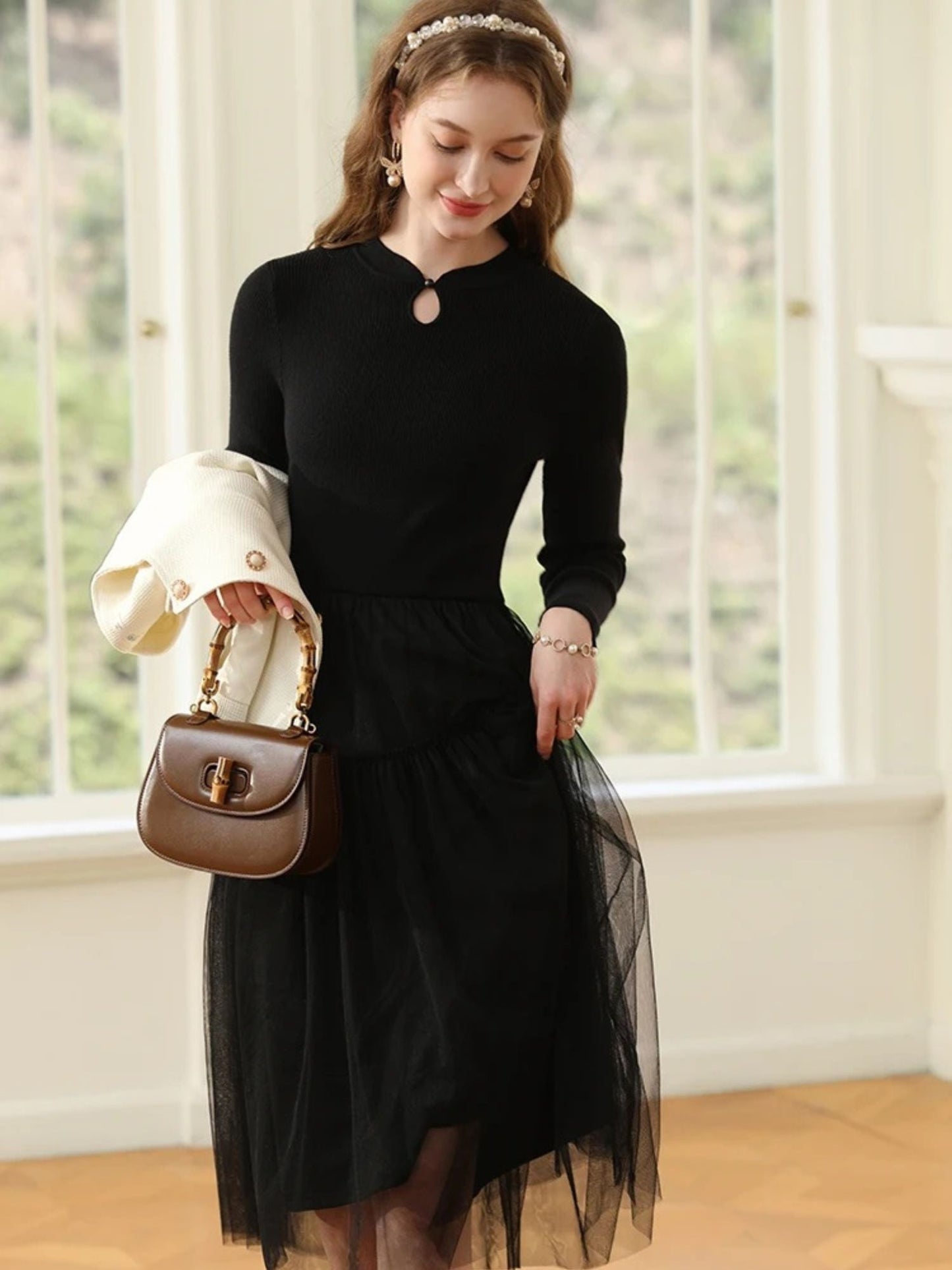 A woman wearing a long-sleeved, knee-length black dress with a tiered tulle skirt and a round neckline with a keyhole detail.