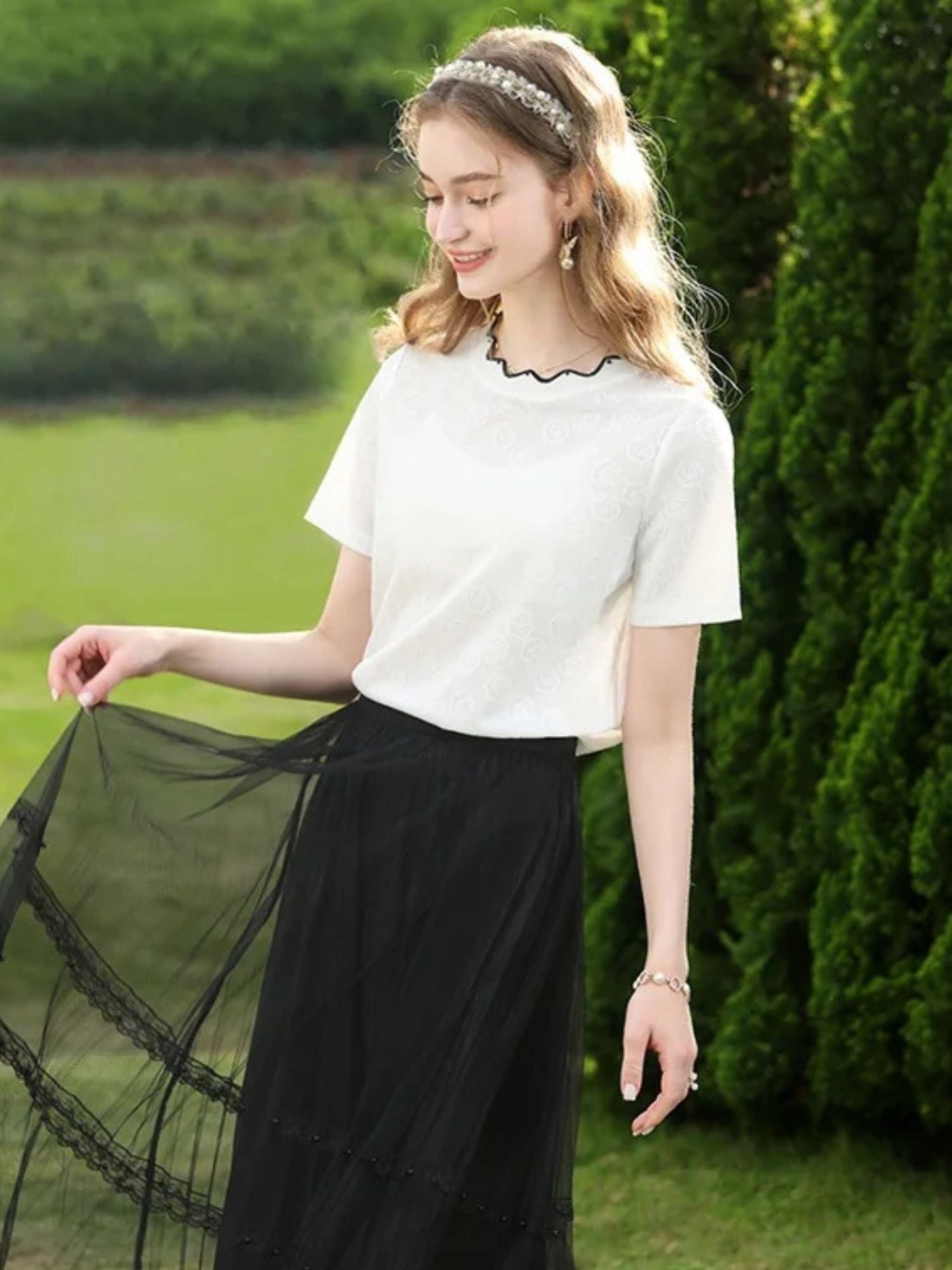 A woman wearing a white short-sleeved blouse with embroidered lace and a crew neckline, paired with a black skirt.