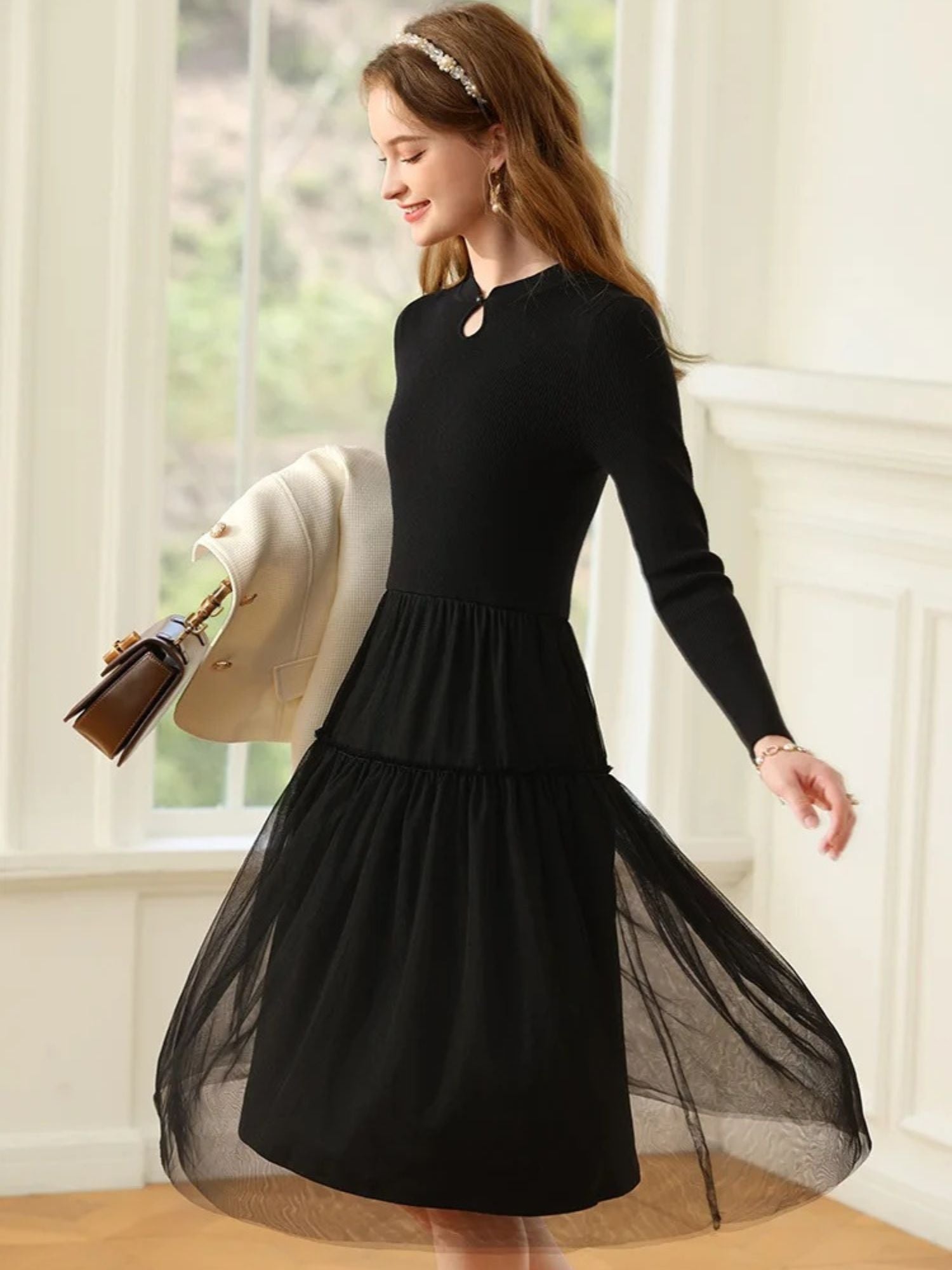 A woman wearing a long-sleeved, knee-length black dress with a tiered tulle skirt and a round neckline with a keyhole detail.