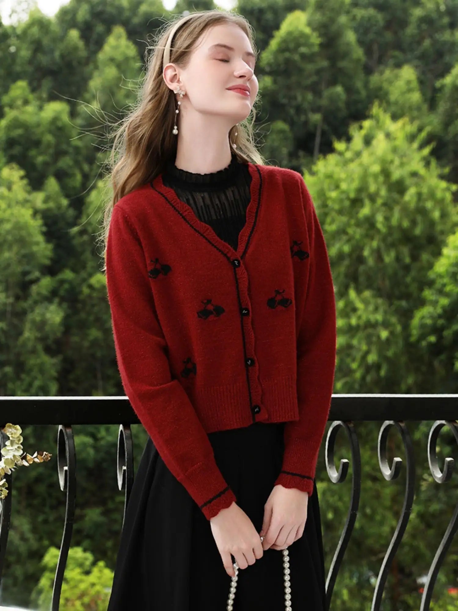 Woman wearing a red cardigan with black details against a green outdoor background