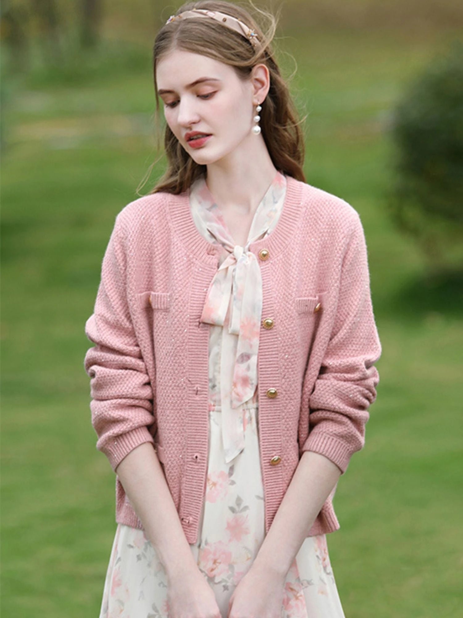Woman wearing a pink cardigan over a floral dress in an outdoor setting