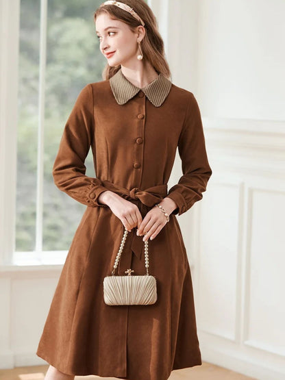 A woman wearing a brown A-line dress with a turn-down collar, long sleeves, front button closure, and tie waist.