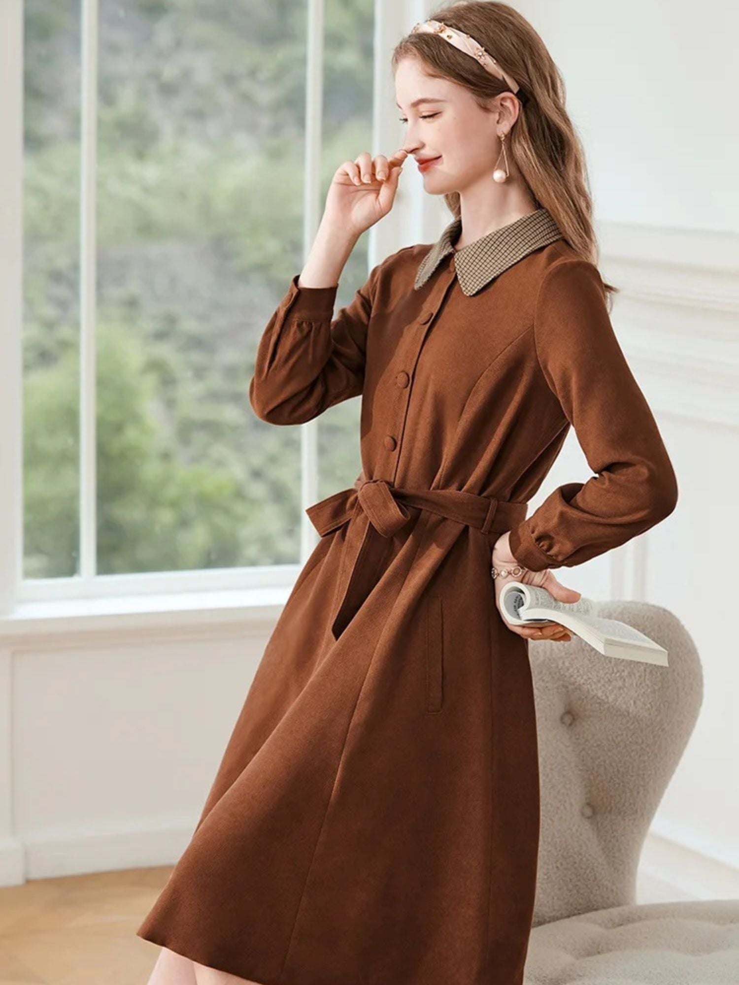 A woman wearing a brown A-line dress with a turn-down collar, long sleeves, front button closure, and tie waist.