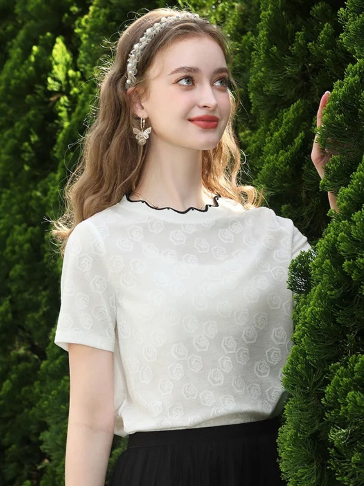 A woman wearing a white short-sleeved blouse with embroidered lace and a crew neckline, paired with a black skirt.