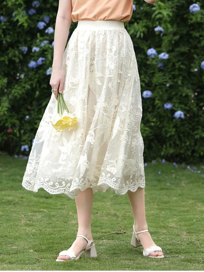 A woman wearing a beige embroidered lace midi skirt with a floral patterned skirt and an orange top, accessorized with a wide-brimmed hat.