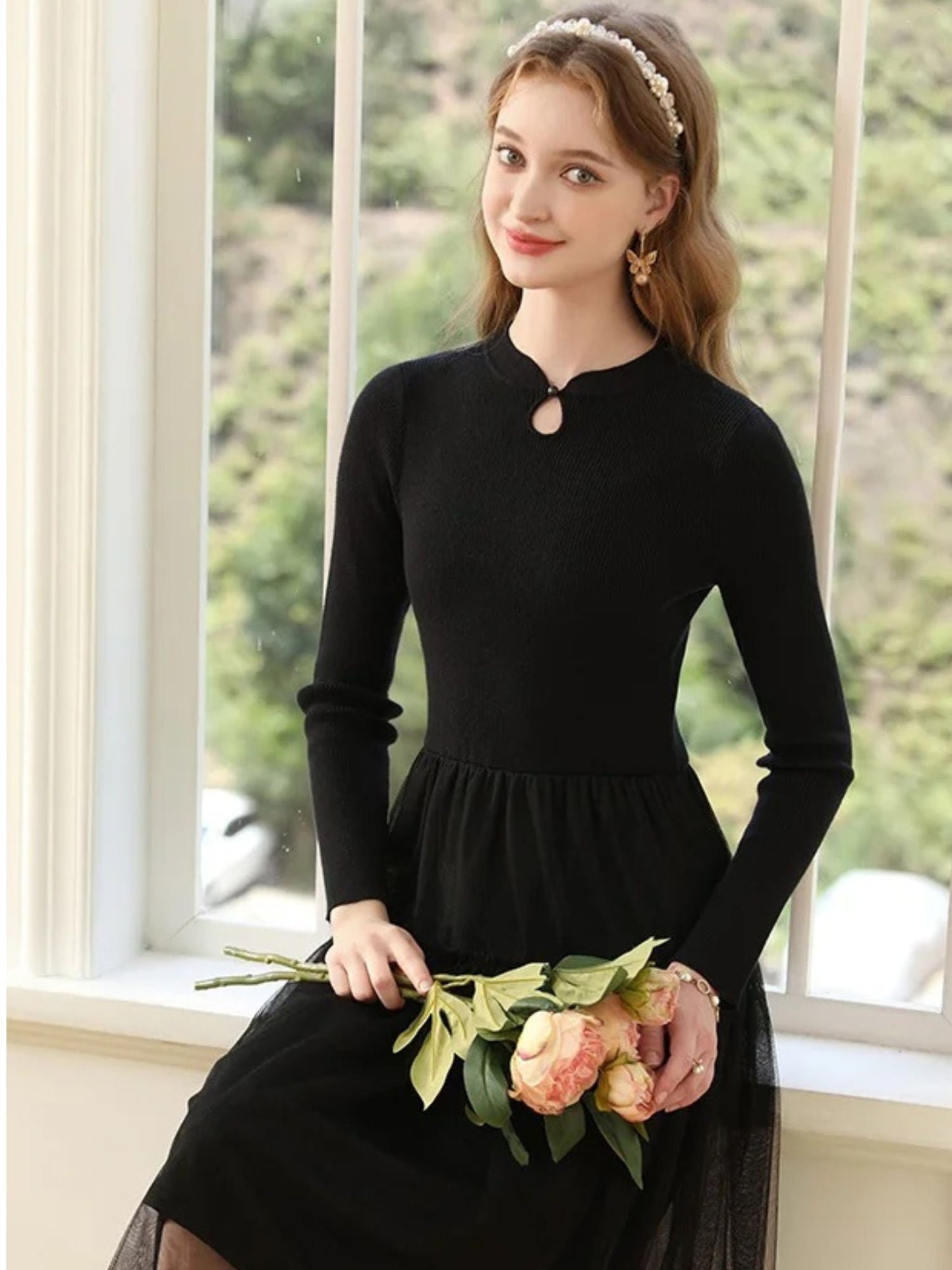 A woman wearing a long-sleeved, knee-length black dress with a tiered tulle skirt and a round neckline with a keyhole detail.