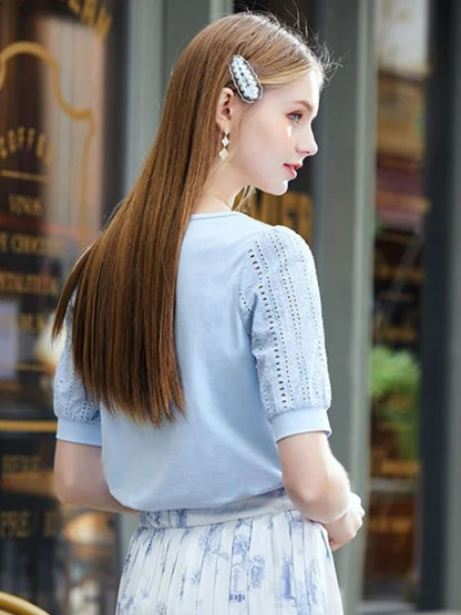 A woman wearing a summer blouse with eyelet ouff sleeves and a square neckline.