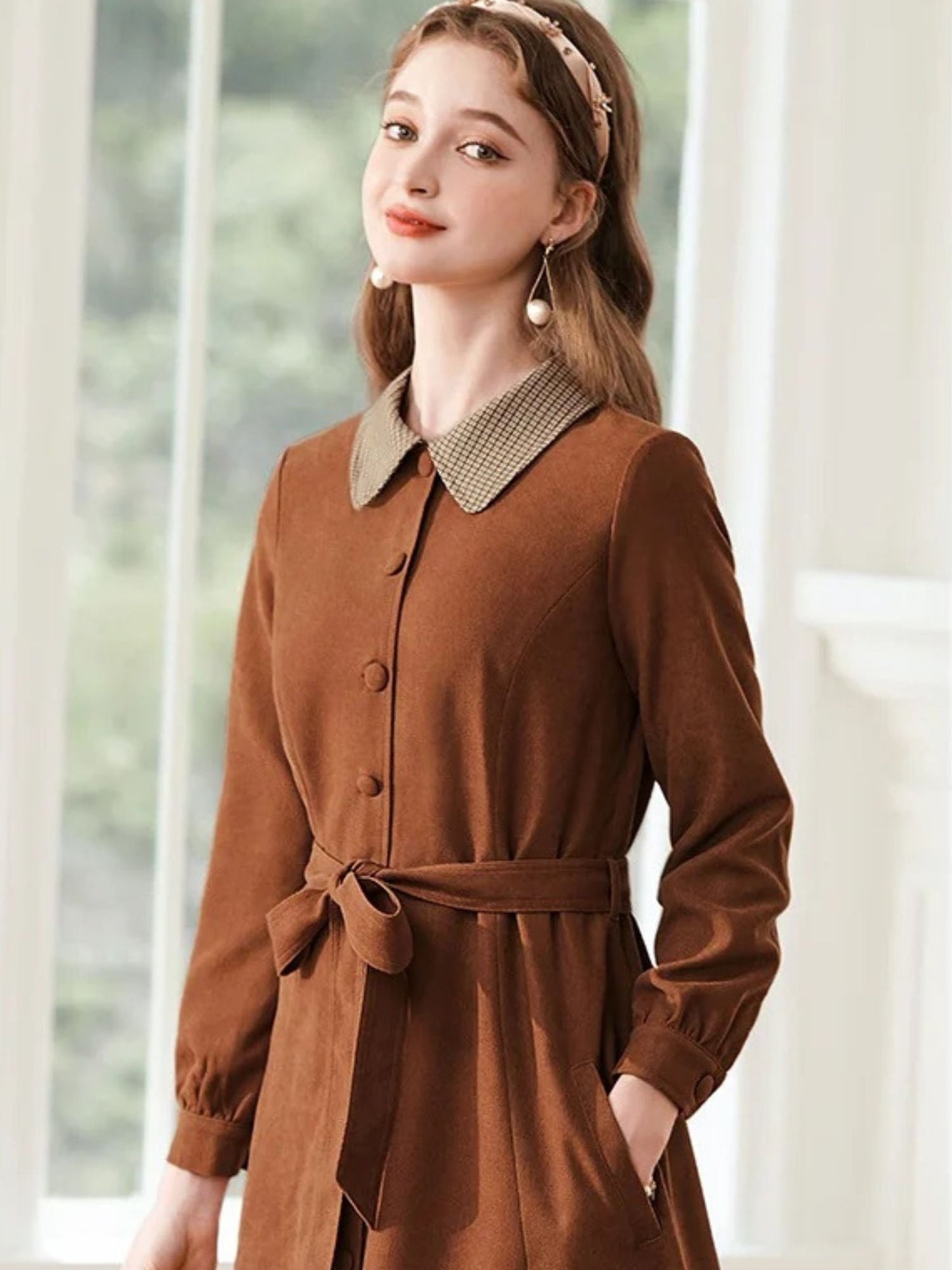 A woman wearing a brown A-line dress with a turn-down collar, long sleeves, front button closure, and tie waist.