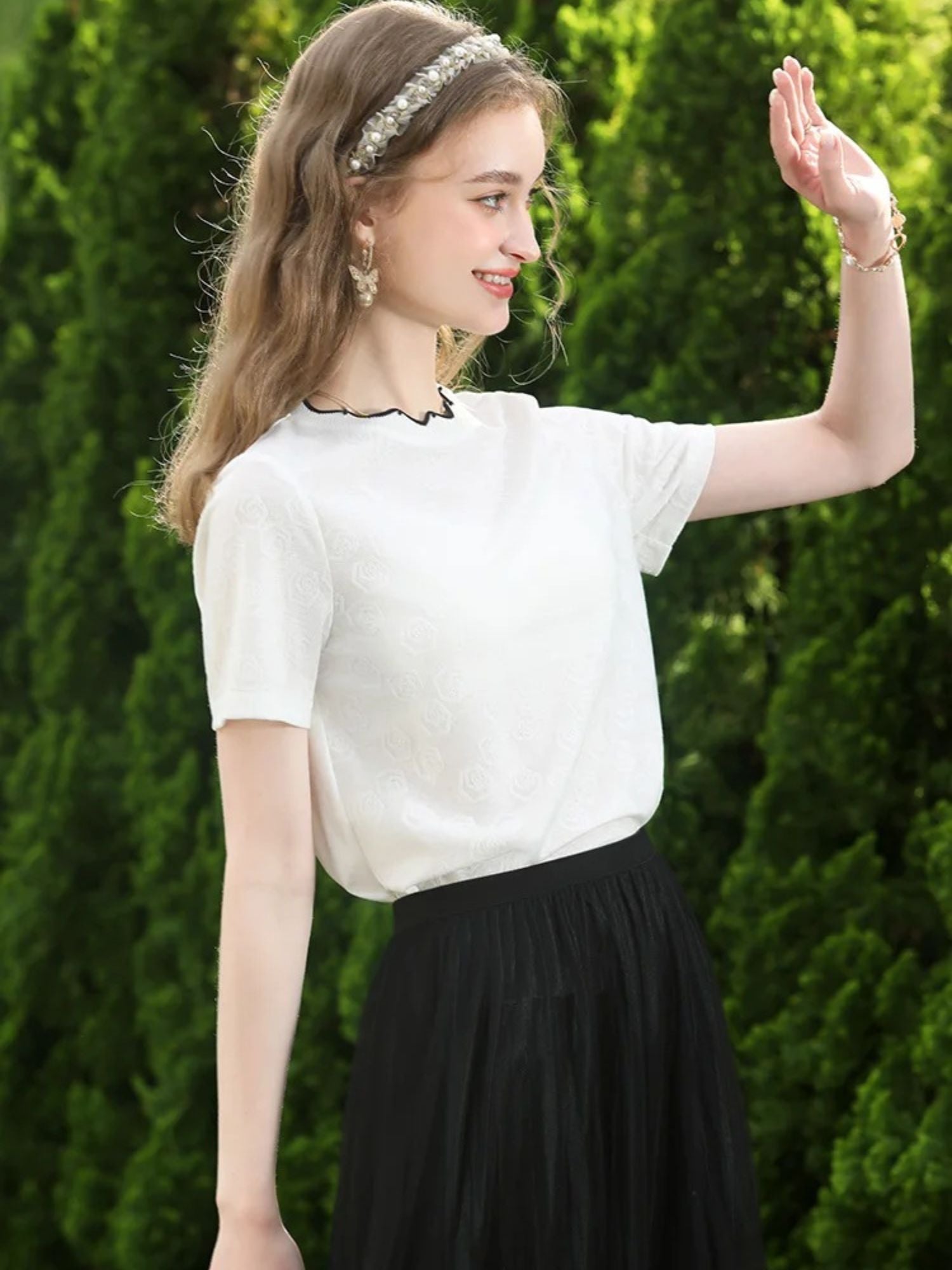 A woman wearing a white short-sleeved blouse with embroidered lace and a crew neckline, paired with a black skirt.