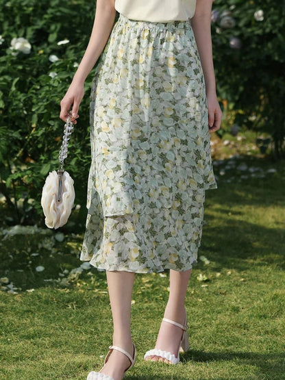 A woman wearing a floral chiffon midi skirt with a high elastic waistband, paired with a plain top, standing in a garden.
