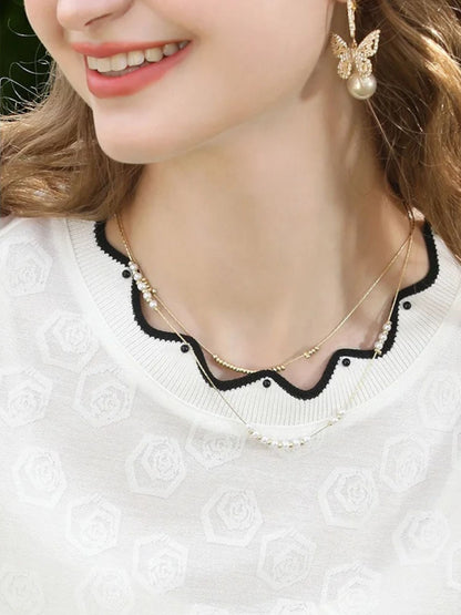 A woman wearing a white short-sleeved blouse with embroidered lace and a crew neckline, paired with a black skirt.