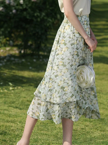 A woman wearing a floral chiffon midi skirt with a high elastic waistband, paired with a plain top, standing in a garden.