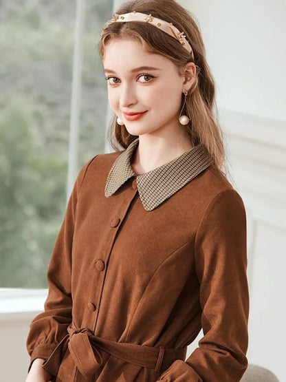 A woman wearing a brown A-line dress with a turn-down collar, long sleeves, front button closure, and tie waist.