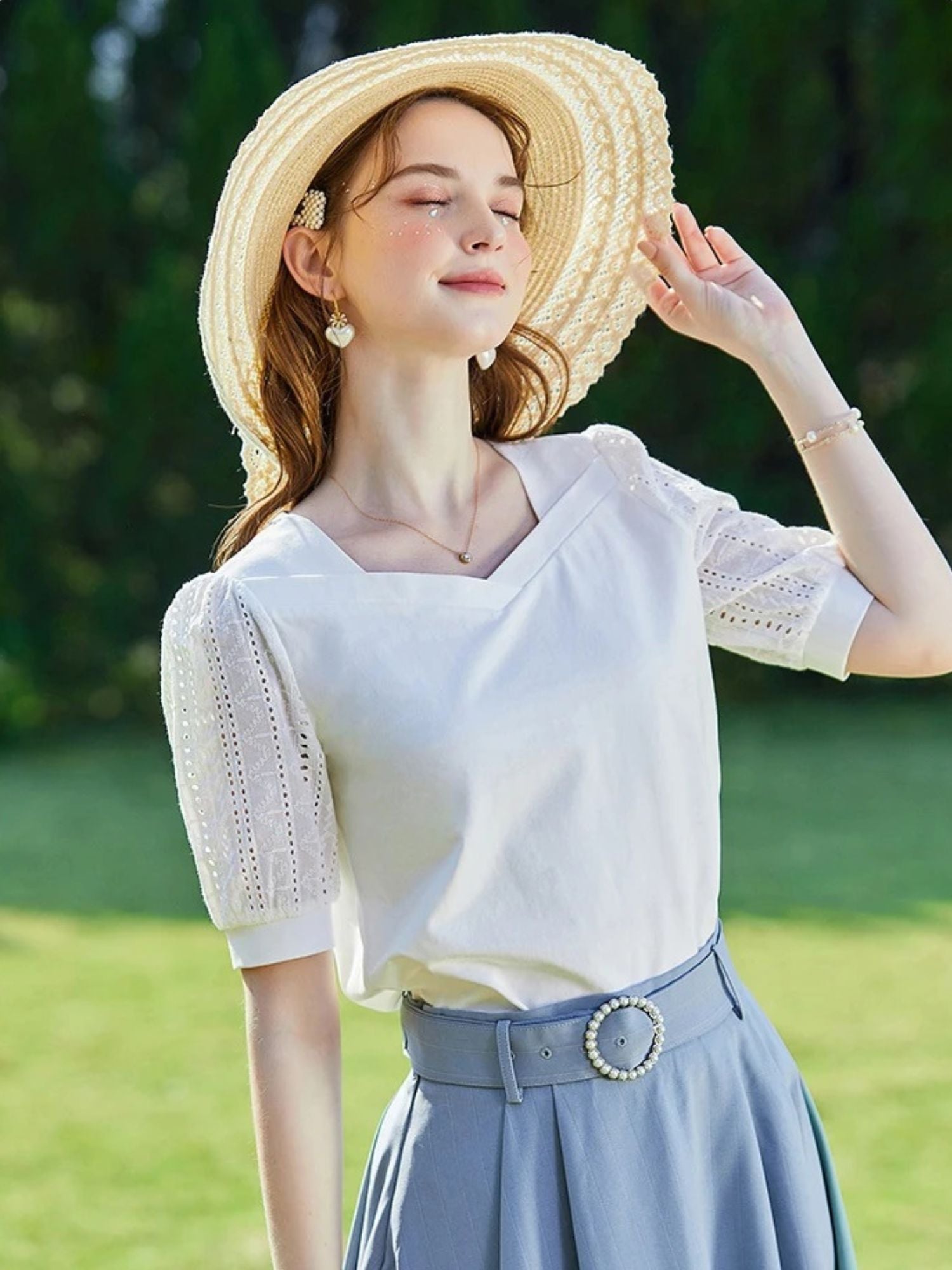 A woman wearing a summer blouse with eyelet ouff sleeves and a square neckline.