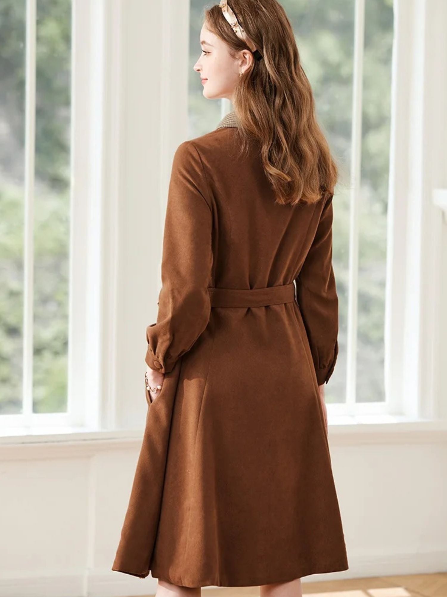 A woman wearing a brown A-line dress with a turn-down collar, long sleeves, front button closure, and tie waist.