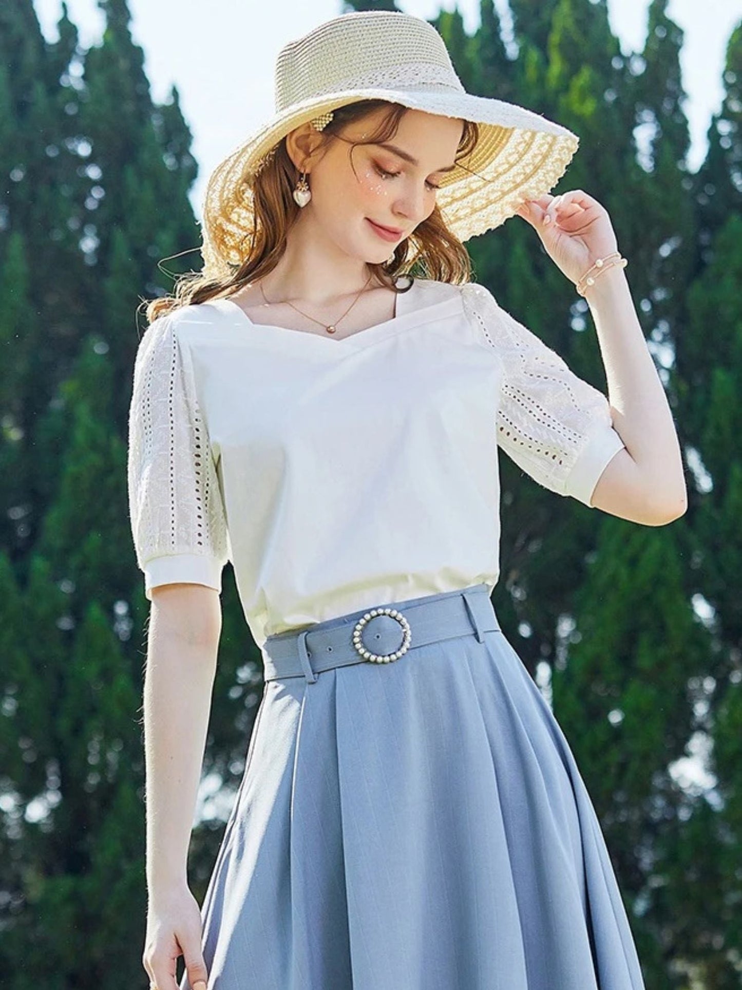 A woman wearing a summer blouse with eyelet ouff sleeves and a square neckline.